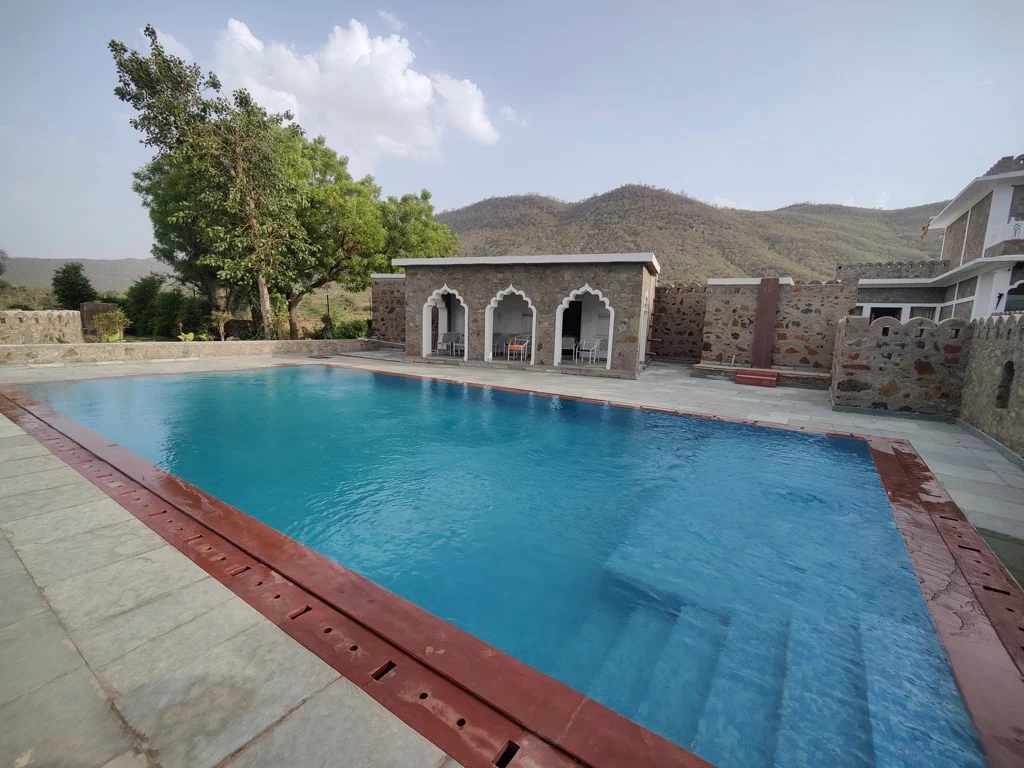 Swimming pool with rain dance overlooking the Aravalli hills by day